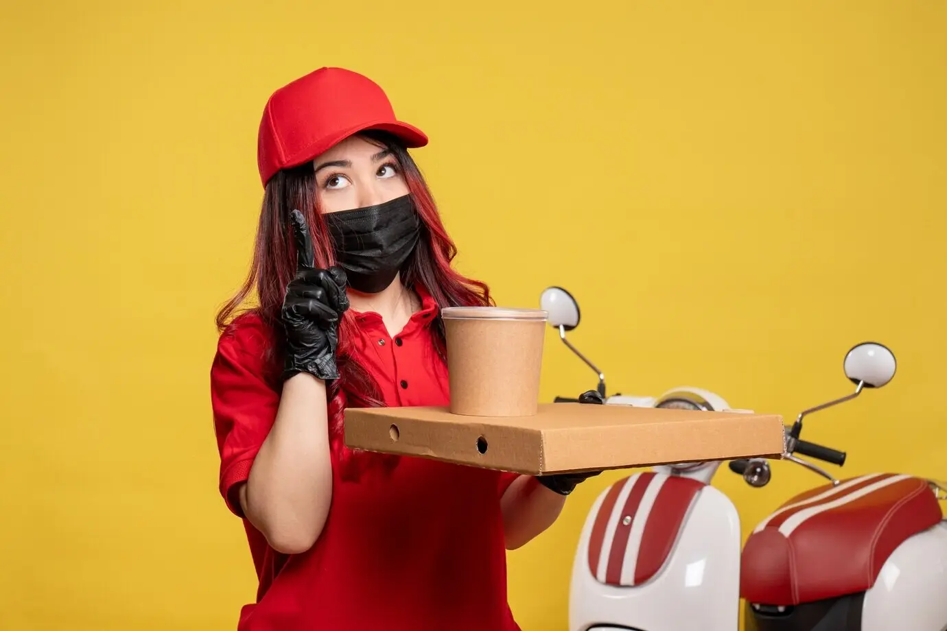 Вид спереди на женщину-курьера в маске с едой для доставки на фоне жёлтой стены.